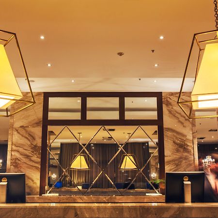 Windsor Marapendi Hotel Рио де Жанейро Екстериор снимка The photo shows a hotel lobby or reception area. There are large geometric light fixtures hanging from the ceiling, providing a warm glow to the space. The reception desk is made of a polished material, likely marble, with decorative elements and two