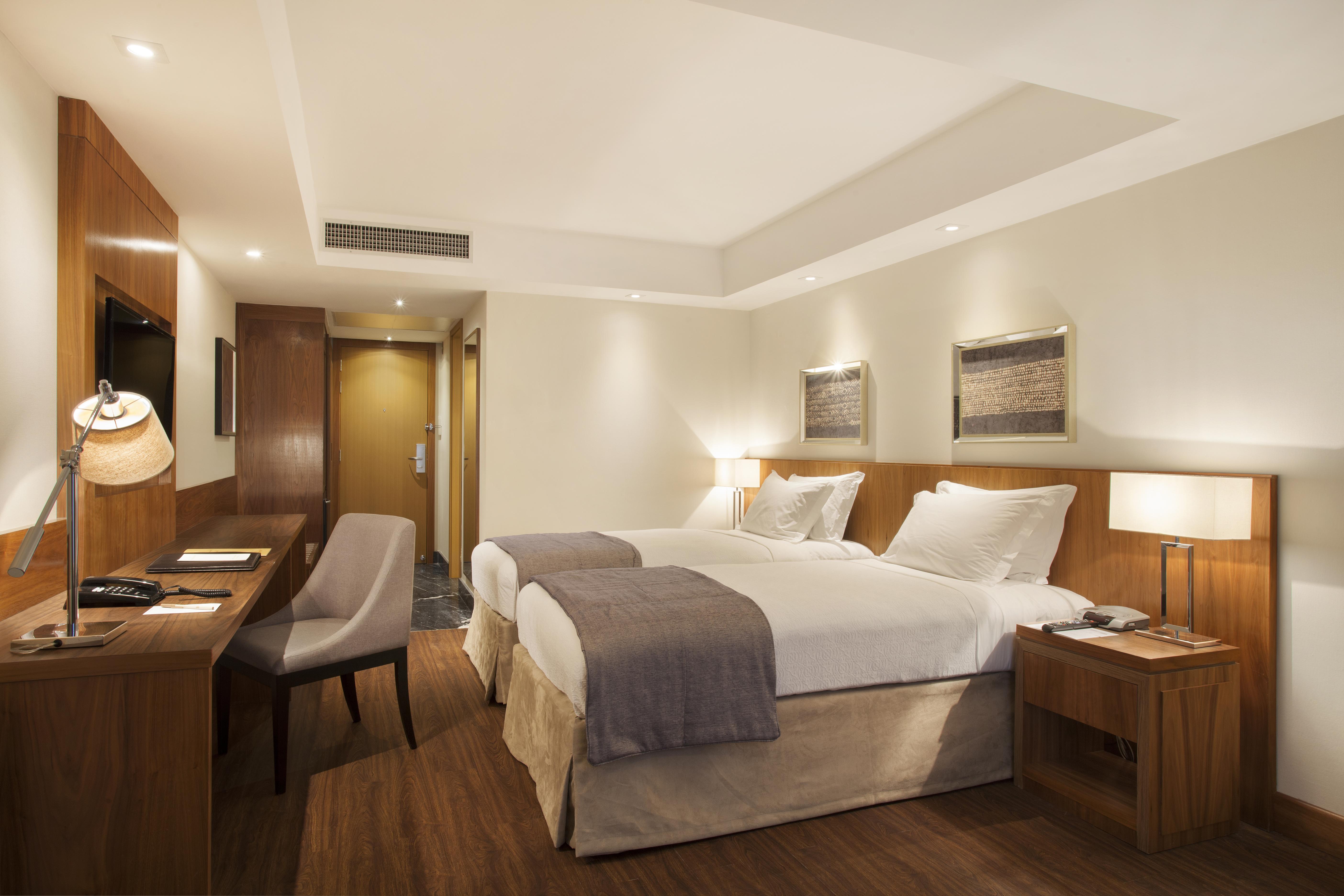 Windsor Marapendi Hotel Рио де Жанейро Екстериор снимка The photo displays a modern hotel room featuring two twin beds with crisp white linens and gray throw blankets. The room has a clean and minimalist design, with wooden accents, including a bedside table and a desk. To the left, there's a small desk a